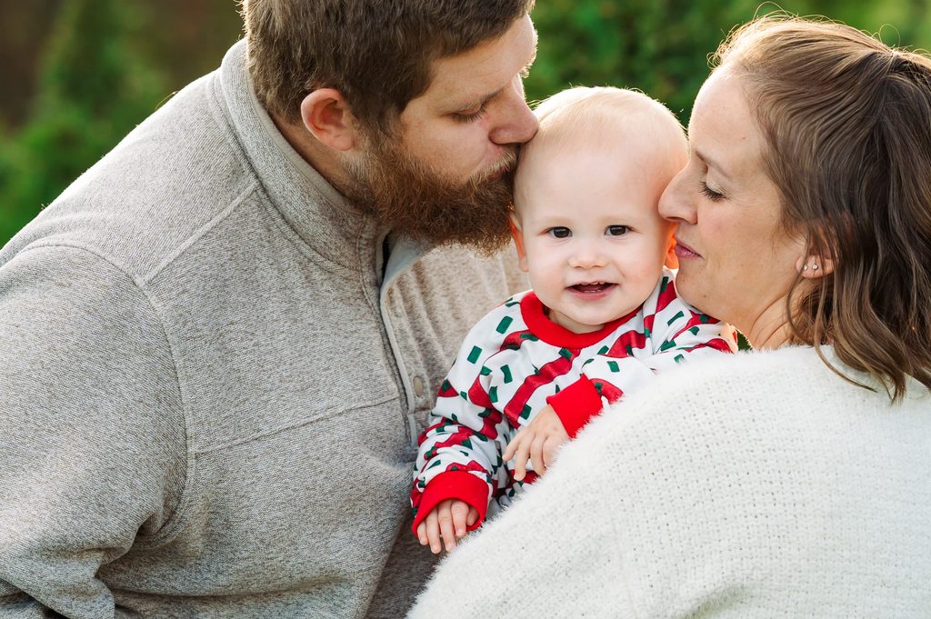 Parents cuddling their baby at a Christmas tree farm mini session at Big Sky Farm near Nashville