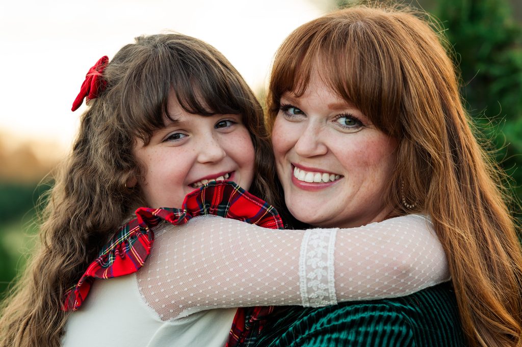 Smiling mom and daughter snuggled close at a Christmas tree farm mini session near Nashville, Tennessee